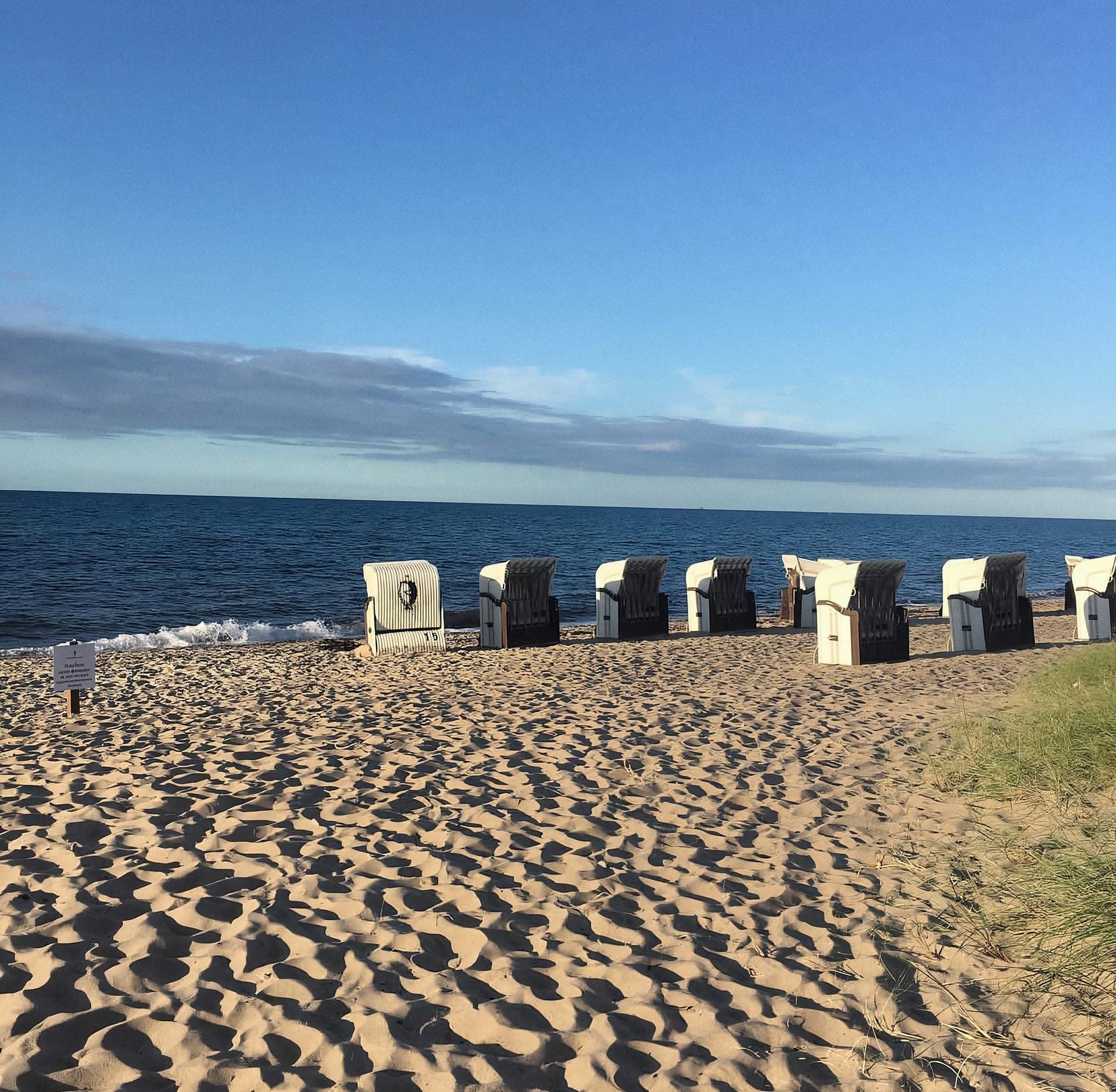 Eine Reihe Strandkörbe im Sand, dahinter die Ostsee unter blauem Himmel