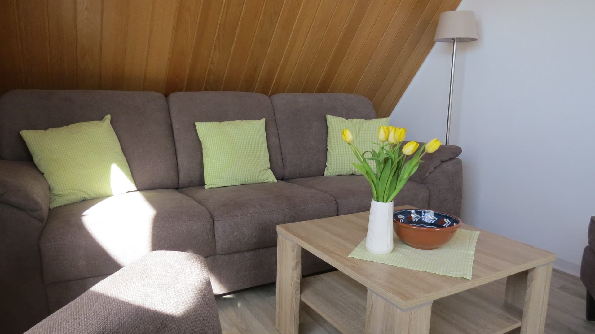 Wohnbereich mit Sofaecke, Sessel und Tulpen auf dem Couchtisch unter der Holzdecke
